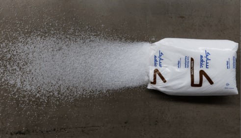 Aufgerissener weißer Sack mit blauer und brauner Aufschrift, aus dem viele kleine weiße Kunststoffgranulat-Kügelchen auf den Boden ausgeschüttet sind.